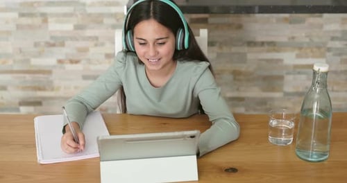 Girl Studies with Tablet and Headphones at Table