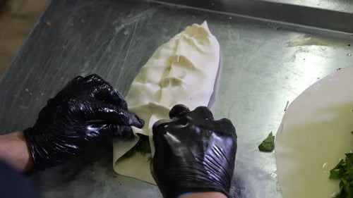 Gros plan d'un chef en gants préparant des tortillas aux herbes Kutabs Gozleme