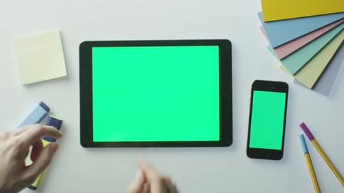 Designer está usando tablet e celular com tela verde.