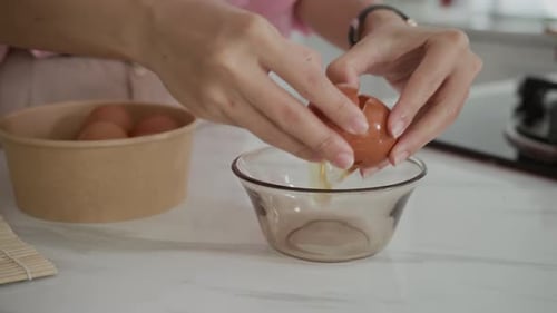 Person Cracking Eggs into Bowl in Kitchen