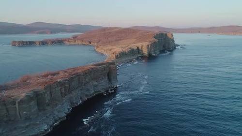 Aerial Drone View of an Ocean Blue Waves Break on High Cliff of a Rocky Mountain During the Sunset