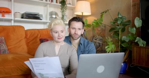 Couple Reviews Financial Documents Together on Laptop Indoors