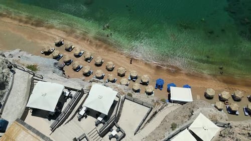 Drone top view: a sandy beach with parasol next to a restaurant terrace, shore of the Mediterranean