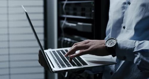 Person Typing on Laptop Near Servers