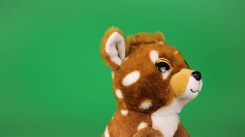 Kuscheliges und flauschiges Plüschtier Rehkitz dreht sich um und schaut sich auf grünem Grund um.
