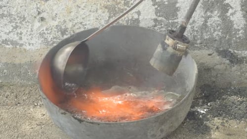 Metal melting in a foundry ladle with a gas torch, industrial setting, close-up
