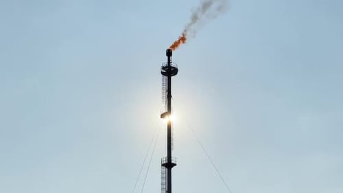 Flare stack refinery burning, giant flame and smokestack, sun behind, clear sky