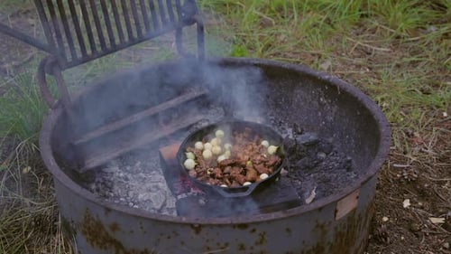 Cooking camping meal of meat and onions in cast iron over camp fire