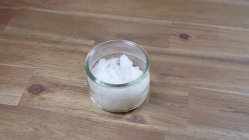 Panning shot of coarse sea salt sitting in a jar. The jar stand on a wooden kitchen counter. Nobody.