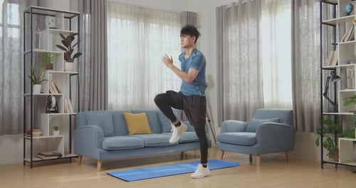 Asian Man In Sportswear Is Energetically Jogging In Place In His Living Room With Modern Interior