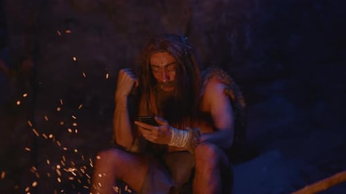 A Caveman Using Modern Technology While Being Situated in a Distinctly Primitive Setting