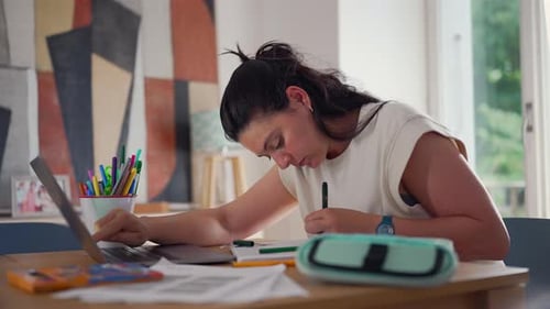 Woman studying in front of a computer, surrounded by documents and stationery, in a home office
