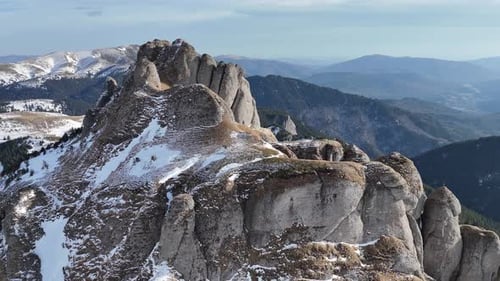 Montagnes enneigées des Ciucas sous un ciel bleu, sommets escarpés avec des forêts de pins en arrière-plan, ciel aérien