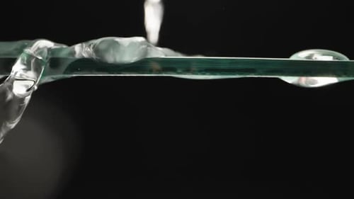 Drops of water roll down the glass, black background. Dolly slider extreme close-up. Laowa Probe