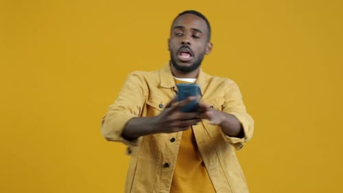 Excited Man Poses with Smartphone on Yellow Backdrop