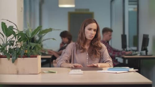 Woman meditating at office desk with coworkers