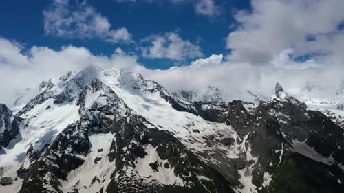 Air flight through mountain clouds over beautiful snow-capped peaks of mountains and glaciers.