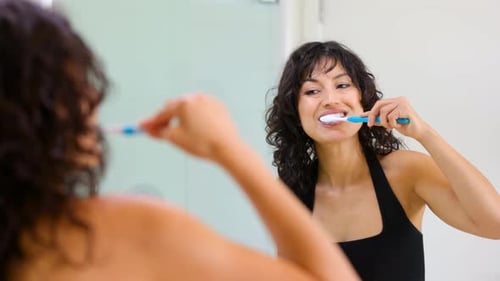Woman Brushing Teeth in Bright Bathroom Mirror