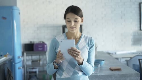 Happy brunette woman uses tablet computer in modern kitchen at home