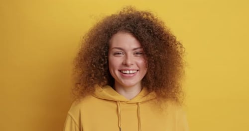 Smiling young woman in yellow hoodie on background