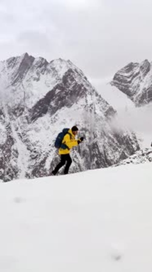 Mountaineer Walking on Snow with Trekking Poles Near Snowy Mountain Range