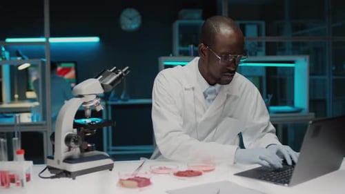 Scientist Using Microscope and Typing in Bright Lab