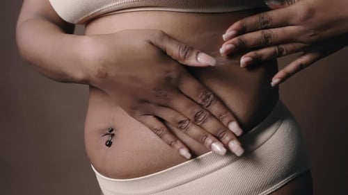 Schwarze kurvige Frau, die Körperlotion auf die Haut aufträgt