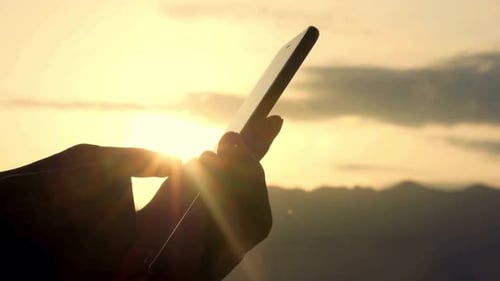 Silhouette of Hands Using Mobile Phone at Sunset