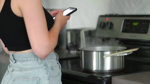 Young Adult Cooking While Using Mobile Phone