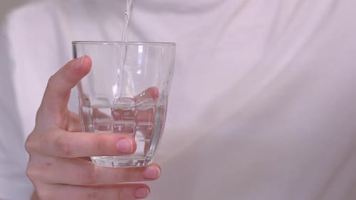 A Hand is Pouring Water Into the Glass, then Drinks it - Close Up