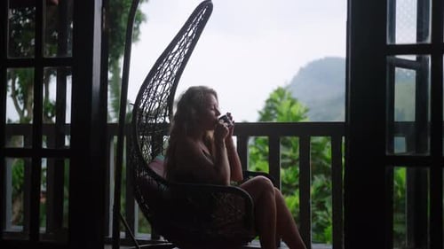 Woman Sips Tea in Hanging Chair Overlooking Mountainous Tea Plantation Luxe Balcony with Green