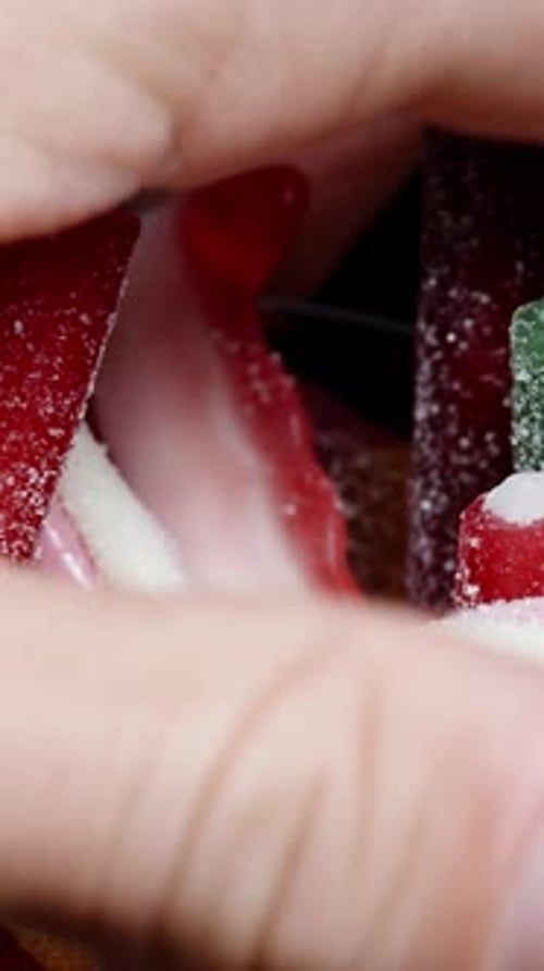 Vertical video. Red gummy candy stick dusted with sugar from the glass filled to the top with a mix