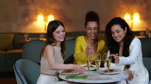 Smiling Young Ladies Laughing Talking Having Dinner in a Restaurant and Clinking Glasses with