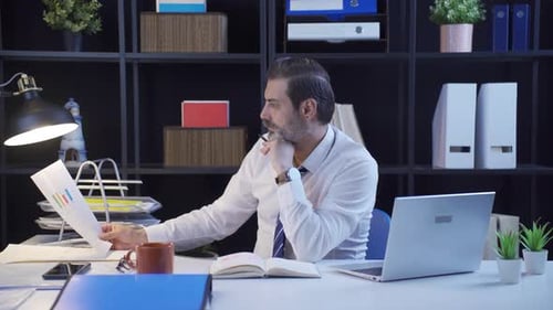 Man Reviews Business Charts and Types on Laptop