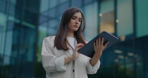 Serious Caucasian Woman Standing in Front of Tall Office and Holding Large Tablet Device with One