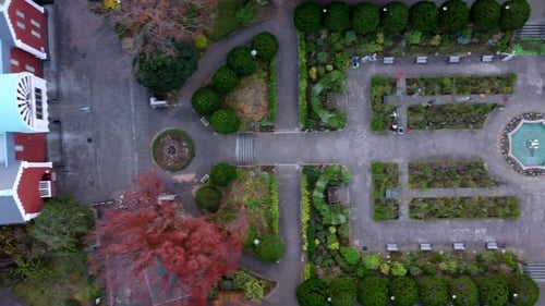 A symmetrical park with a central fountain and parked cars, shot during the day, aerial view