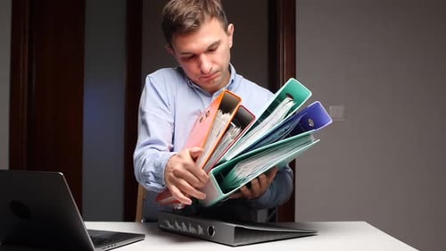 Young Man Stacks Binders on Desk at Work