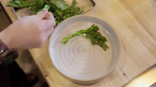 Close-up of cooked vegetables being plated in a restaurant kitchen. Chef finishes a hot dish with