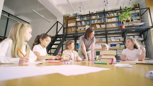 Elementary School Students Sit at a Round Table in an Art Class and a Young Modern Teacher in
