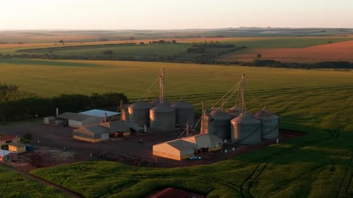 Aerial view of grain silo farm at sunset surrounded by vast farmland