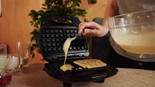 Woman Sitting at the Table at Home in the Kitchen and Preparing Dough for Waffles Breakfast Pours