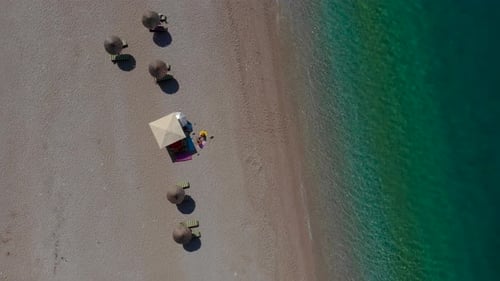 Beach umbrellas on sand washed by calm clear water of turquoise sea in Mediterranean, top down view
