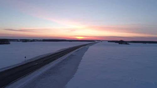 Aerial Wide Shot of an Intercity Road with Traffic Among the Fields Covered with Snow on the Sunset