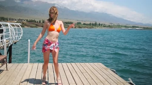 The young beautiful girl dances in swimwear dress on the pier on sea. Slow motion. Wide shot.
