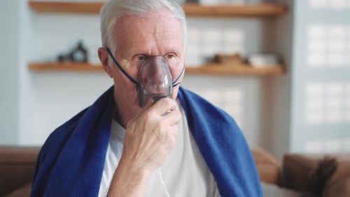 Portrait d'un vieil homme inhalant de l'oxygène concentré provenant d'un nébuliseur à la maison pour guérir et soulager la pneumonie