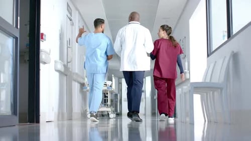 Diverse male and female doctors discussing work and walking in corridor at hospital, slow motion