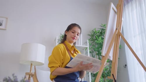 Asian young talented woman artist coloring on painting board in house.