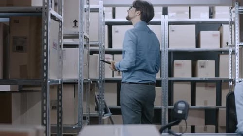 Warehouse Worker Uses Digital Tablet Computer to Checks Stock on Shelves For the Right Cardboard Bo