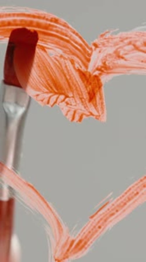 Vertical video. The artist fills in the heart shape on the glass with red color. Low angle.