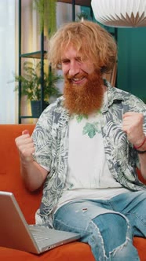 Man celebrates while using a laptop on a couch